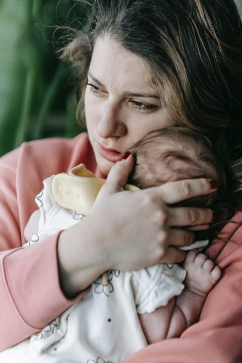 a mother cradling her baby against her chest, looking lost and sad.