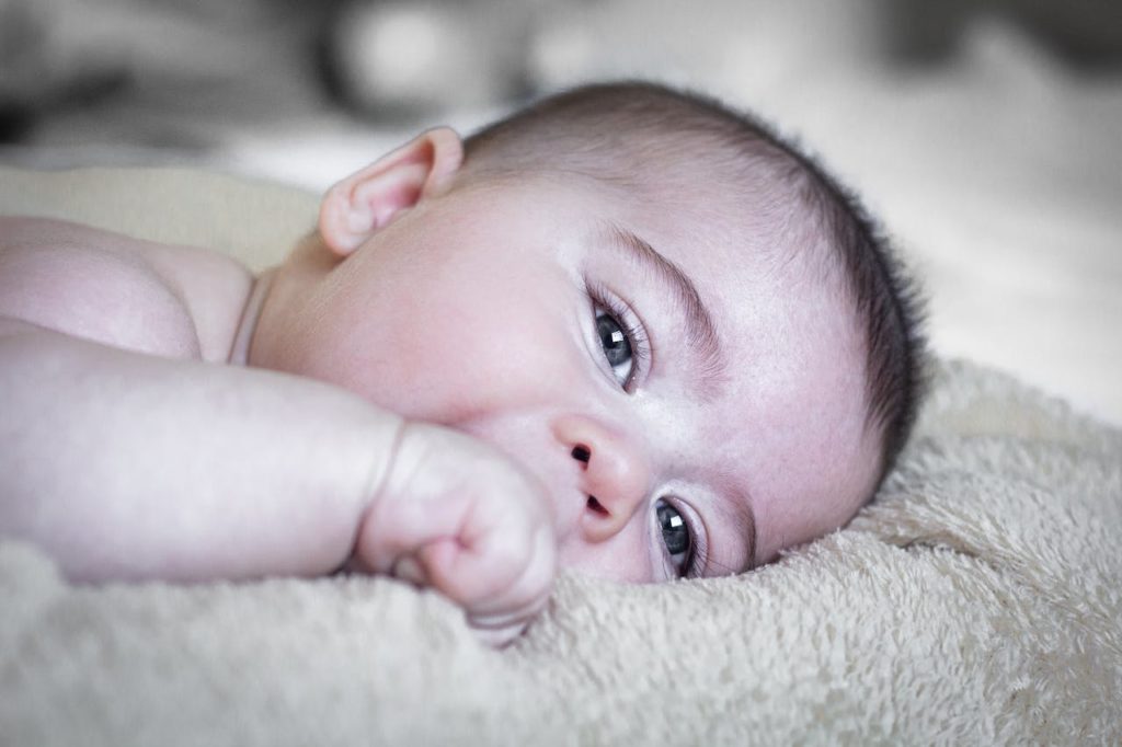 A little baby looking out at the camera, chewing on a fist.
