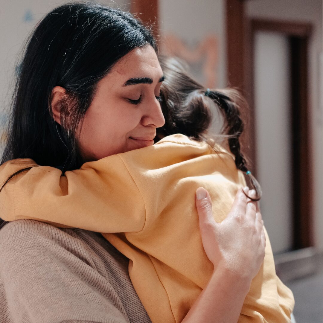 A mother cry-smiling as she holds her child close in a hug.