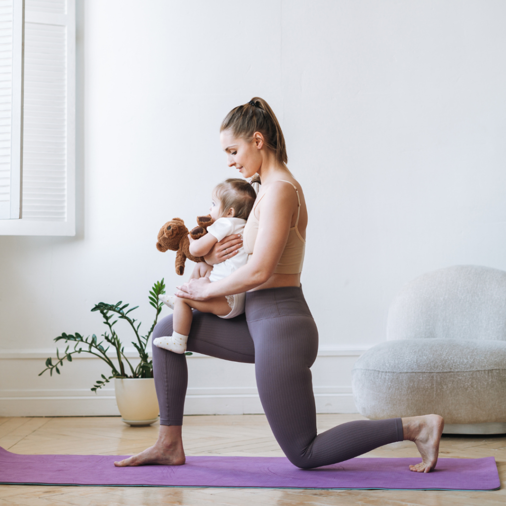 A young mother poses in a lunge while her young child sits on her lap, held in her arms. 