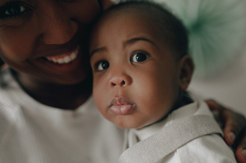 A mother smiles as she holds her child, who looks with big eyes up at the world. 